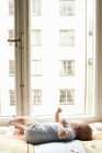 Baby girl lying down and looking through window — Stock Photo