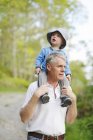 Чоловік, що носить онука на плечах, зосередьтеся на передньому плані — стокове фото