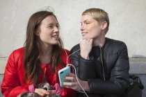 Duas mulheres ouvindo música no smartphone, foco em primeiro plano — Fotografia de Stock