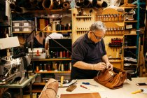 Homem sênior em óculos trabalhando em oficina de couro — Fotografia de Stock