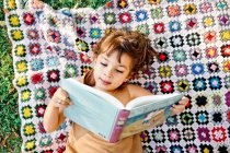 Mädchen liest Buch auf Picknickdecke — Stockfoto