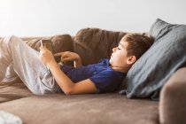 Мальчик на диване играет с планшетным компьютером — стоковое фото