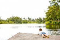 Fille couchée sur une jetée près d'un lac — Photo de stock