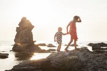 Girl walking with brother on coastal rocks — Stock Photo