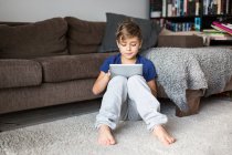 Мальчик на полу играет с планшетным компьютером — стоковое фото