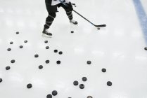 Junge Eishockeyspielerin mit vielen Pucks auf der Eisfläche — Stockfoto