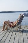 Mulher madura tomando banho de sol em cadeira de praia perto do mar — Fotografia de Stock