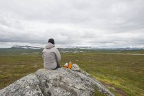 Frau mit isoliertem Getränkebehälter sitzt auf Felsen und blickt auf Berge — Stockfoto