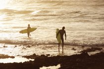 Surfistas en la playa al atardecer, enfoque selectivo - foto de stock