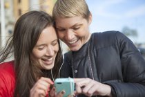 Zwei Frauen hören Musik auf dem Smartphone, konzentrieren sich auf den Vordergrund — Stockfoto