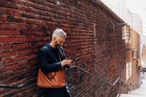 Человек у стены с брикетом на смартфоне — стоковое фото