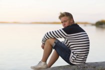 Adolescente sentado na rocha pela água — Fotografia de Stock