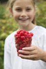 Girl with cup of raspberries looking at camera — Stock Photo