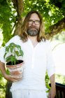 Mann steht mit Topfpflanze und blickt in Kamera — Stockfoto