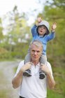 Man carrying grandson on shoulders, focus on foreground — Stock Photo