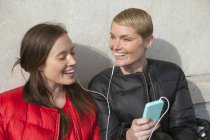 Дві жінки слухають музику на смартфоні, сидячи на сходах — стокове фото
