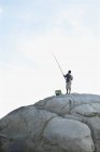 Человек рыбачит на скале в Кэмпс-Бэй в Кейптауне — стоковое фото