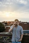 Junger blonder Mann raucht bei Sonnenuntergang auf dem Dach — Stockfoto