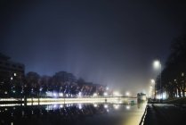 Illuminated riverbank at night, buildings exterior at background — Stock Photo