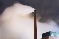 Дым выходит из дымовой трубы на заводе ночью — стоковое фото