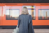 Вид сзади на женщину в пальто, стоящую на станции метро — стоковое фото