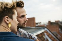 Young couple side by side on rooftop against cloudy sky — Stock Photo