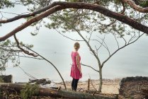 Jeune femme en robe rose regardant l'océan — Photo de stock
