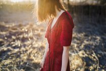 Jovem mulher de cabelo vermelho em vestido vermelho de pé à luz do sol — Fotografia de Stock