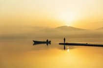 Silhouettes of two people in boat and on jetty — Stock Photo
