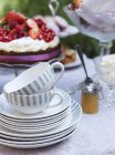 Teetassen und Teller auf dem Tisch mit Kuchen im Hintergrund, Fokus auf Vordergrund — Stockfoto