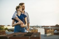 Молодая пара обнимается, стоя на крыше — стоковое фото