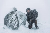 Junge Backpackerin kniet bei Schneesturm neben Felsen — Stockfoto