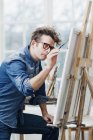 Man wearing eyeglasses painting at easel — Stock Photo