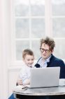 Padre e hijo vistiendo ropa formal usando laptop y sonriendo - foto de stock