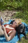 Mulher deitada na praia com cão e livro de leitura — Fotografia de Stock