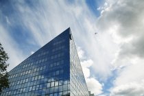 Fachada edifício moderno com avião em movimento no céu nublado — Fotografia de Stock