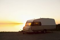 Reboque de acampamento estacionado junto ao lago ao pôr do sol — Fotografia de Stock