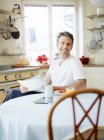 Mann mit Zeitung am Frühstückstisch sitzend und lächelnd — Stockfoto