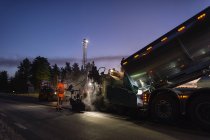 Tres trabajadores manuales reparando la carretera por la noche - foto de stock