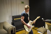 Молодий чоловік грає на гітарі, зосереджується на передньому плані — стокове фото