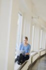 Junge Frau benutzt Laptop an der Universität auf Fensterbank — Stockfoto