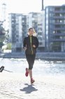 Woman in sportswear running along embankment — Stock Photo