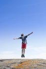 Rückansicht eines Jungen, der vor blauem Himmel auf einen Felsen springt — Stockfoto