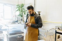 Small business owner at coffee roaster shop using smartphone — Stock Photo