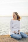 Молодая женщина, сидящая у моря в Карлскруне, Швеция — стоковое фото
