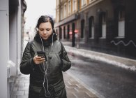 Жінка слухає музику на смартфоні на вулиці, фокус на передньому плані — стокове фото
