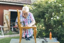 Senior man repairing chair outdoors in Kvarnstugan, Sweden — Stock Photo