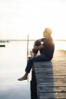 Людина сидить на пірсі на заході сонця в Блекінге, Швеція — стокове фото