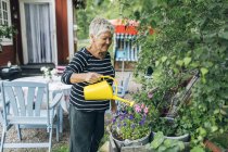 Femme âgée arrosant le jardin, se concentrer sur le premier plan — Photo de stock