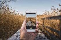 Male hand holding smart phone, taking photo of winter field — Stock Photo